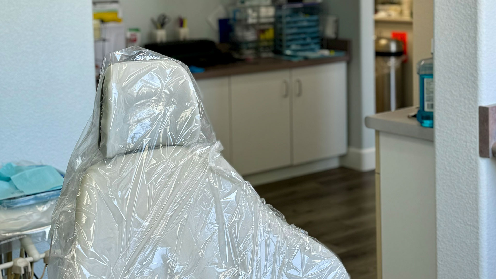 The image shows a dental chair covered with plastic, situated in what appears to be a dental office.