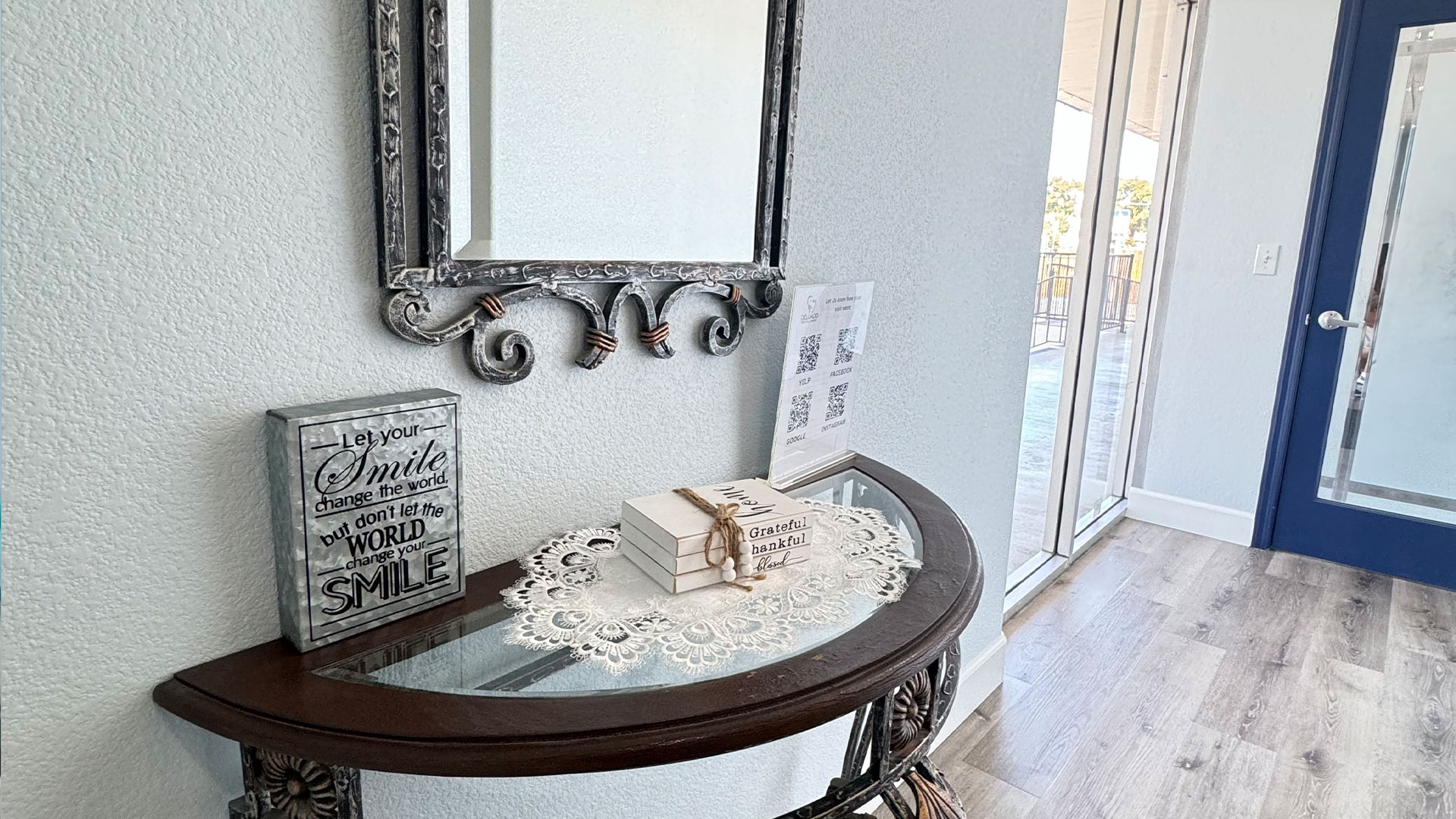 An interior photograph of a room with a framed mirror, lace doily, and glass table displaying cards  the image is taken from a low angle.