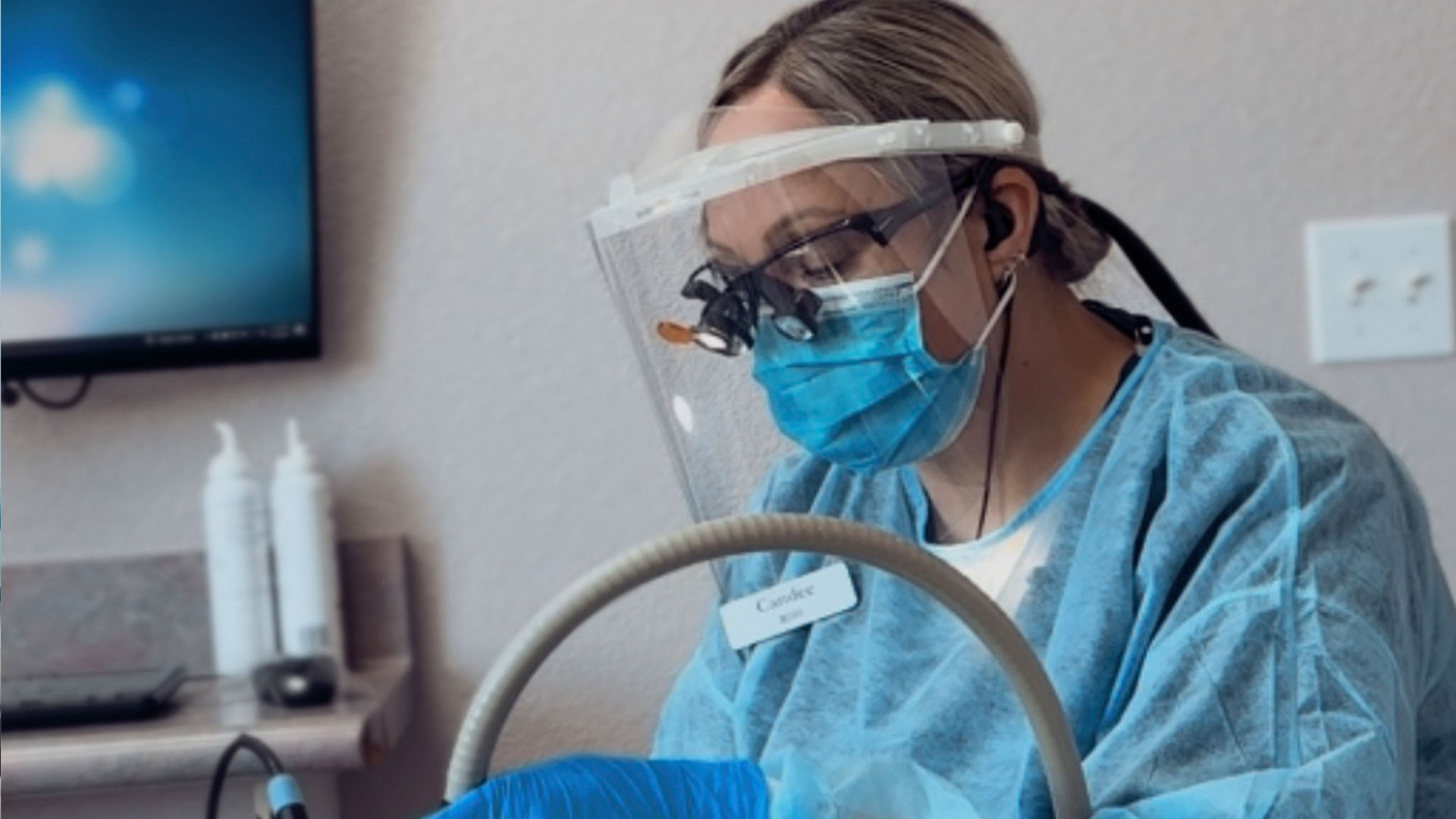 A woman in a medical gown and face mask is operating medical equipment, possibly conducting a test or procedure.