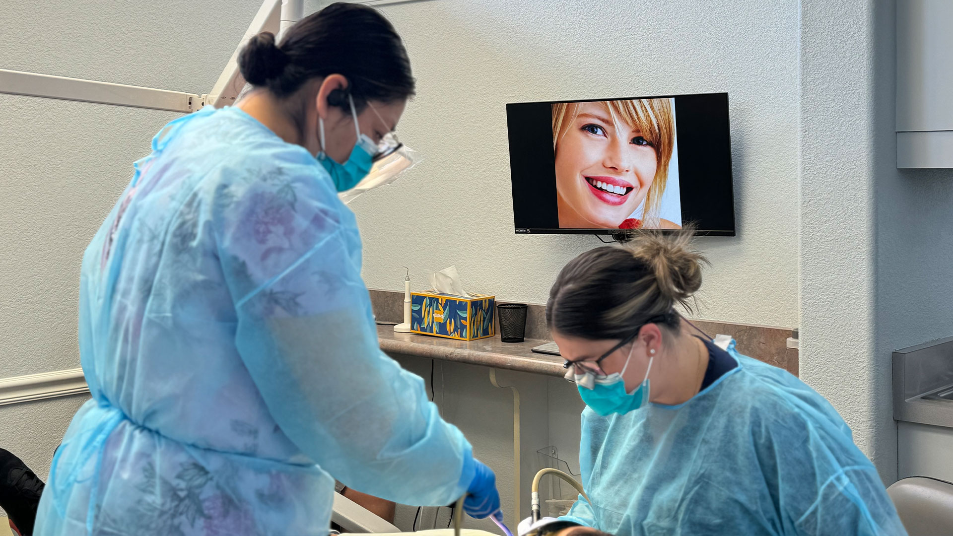 Two dental professionals wearing protective gear, working in a dental office setting.