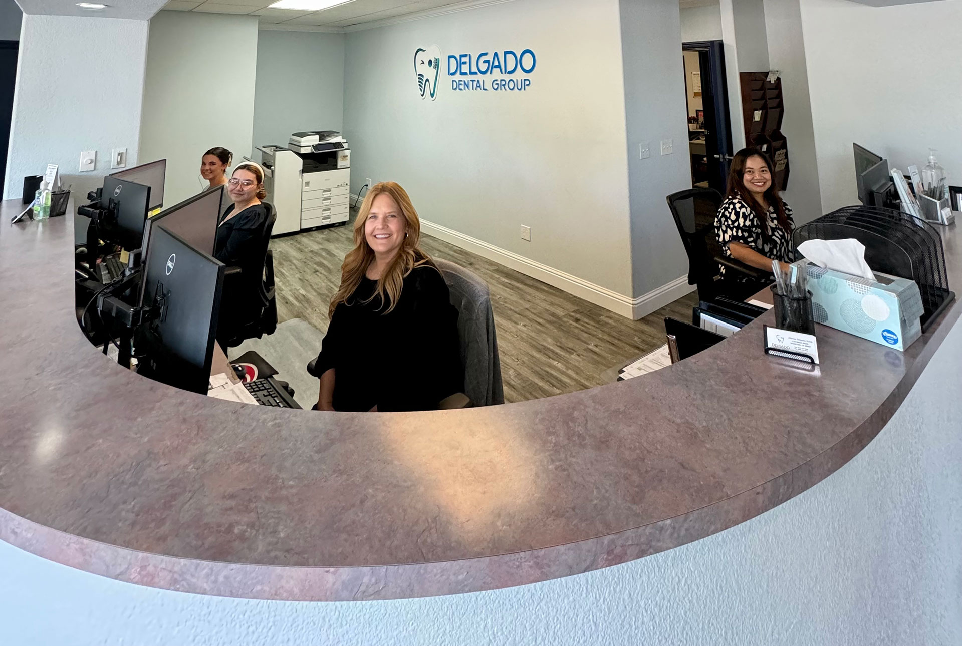 Three individuals seated at a counter within an office space, with one person standing behind the counter.