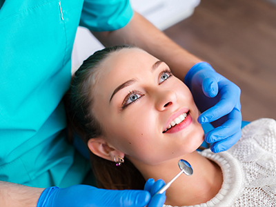 A woman receiving dental care with a smiling expression, assisted by a dental professional in a clinical setting.