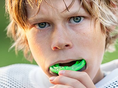 The image shows a young male with blonde hair, wearing a sports jersey, holding a green object to his mouth.